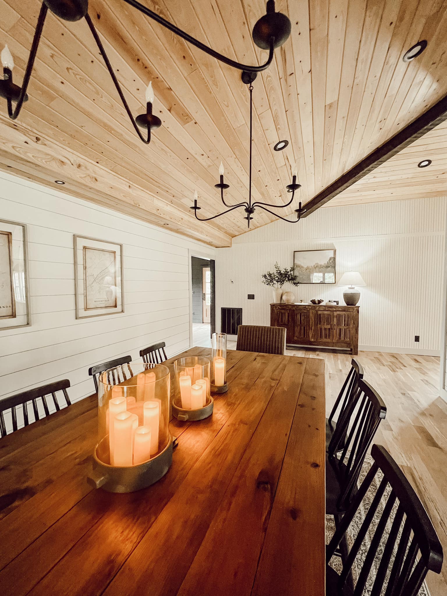 Farmhouse dining room with a long wood table, lit candle centerpieces, black chandelier, dark wood chairs, and a wood-plank vaulted ceiling.