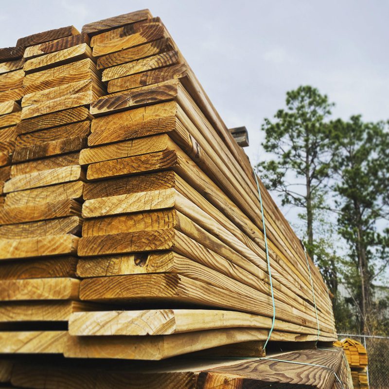 Stack of deck boards with trees and blue sky in the background